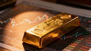 Gold bar with blurred financial charts in background.